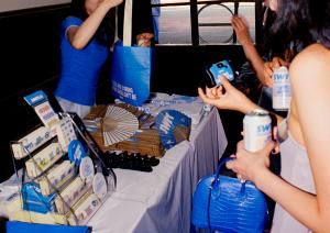 Guests interacting at SWRL's merch booth during the NYC launch party, picking up branded fans, cameras, and sipping cans of makgeolli seltzer.