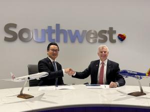 A professional photo of China Airlines President Kevin Chen and Southwest CEO Bob Jordan shaking hands at a conference table after signing a Memorandum of Understanding (MoU). Two model airplanes, one from each airline, are on the table in front of them. 