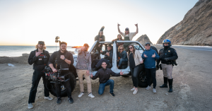 Ventura County Coast team and agency crew standing alongside local cast members during a commercial shoot on Pacific Coast Highway, with ocean views and camera gear in the background.