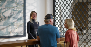 Local actor portraying a business traveler checking into a stylish Ventura County Coast hotel lobby, greeted by a smiling front desk staff member during the filming of a commercial scene