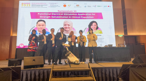 Group photo beside the RevitaVivante™ ProMax FES-cycling system; Even Koh is fourth from the left, with Professor Ir Dr Nur Azah Hamzaid standing immediately to his right, against a conference backdrop.