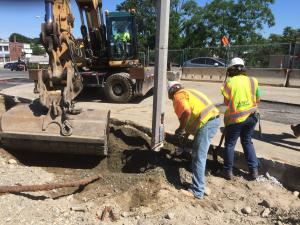 Construction workers and an excavator digging near a utility pole, illustrating the critical need for careful excavation to prevent damage to underground infrastructure and ensure worker safety.