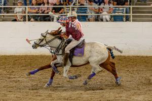 Two male polo players shoulder for a shot on the ball on horseback during polo game