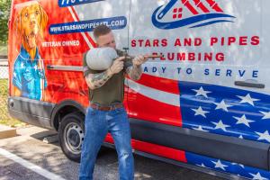 Stars and Pipes Plumbing Atlanta owner Sean Nelson holding a thermal expansion tank in front of the company van