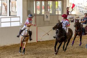 two women arena polo players give each other a mallet high five after scoring a goal