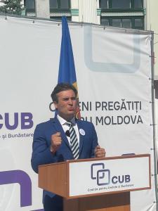 Adriano Dulgher, Vice President of CUB (Coaliția pentru Unitate și Bunăstare), speaks at a podium during a political event in Chișinău, Moldova, addressing citizens about unity, prosperity, and European values. The CUB logo and Moldovan flag are visible i