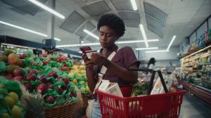Woman in grocery store enters EBT card number into phone while holding groceries and EBT ard