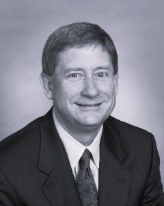 Professional headshot of John West in black and white