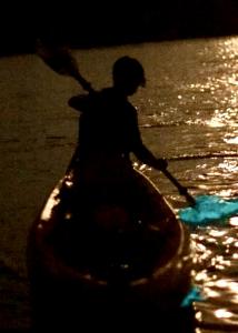 Kayaker paddling through glowing bioluminescent waters on Florida’s Space Coast at night.