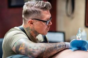 Elvis Tattoo Shop Introduces EU REACH-Compliant Inks and Spot-Testing 15 Tattoo artist working on a client’s upper arm under a ring light at Elvis Tattoo Shop
