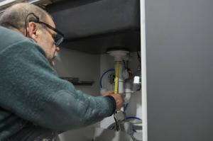 Plumber measuring pipe under kitchen sink to install a sink siphon connected to the garbage disposal unit