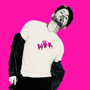 DJ SïNR in black and white photo, posing in an artistic model like form looking straight at the camera, full body. The image of the DJ is cut out and placed on a bright pink background. The logo of the DJ features in the same bright pink on the front of t