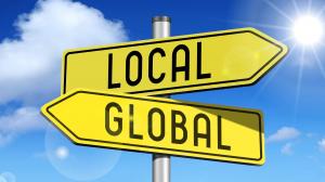 Yellow street signs pointing in opposite directions labeled "Local" and "Global," symbolizing the strategic choice brands must make when expanding internationally.