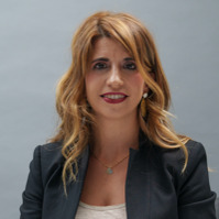 Portrait of Adelaide Raia, General Manager of Alfasigma Consumer Health Business Unit, wearing a dark blazer and smiling in front of a neutral background.