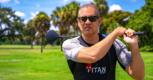 Man in sunglasses wearing a Titan Body EMS training suit holding a golf club across his shoulders on a sunny day at the golf course.