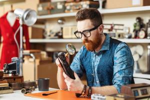 Young business owner working in his  shop, he is checking an old sculpture using a magnifier, he sells vintage and second-hand items