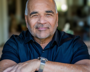Picture of a man smiling and sitting at a desk with his arms on the table.