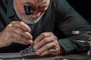 Watchmaker repairing watches looking through magnifying glass monocular. Professional senior watch fixer in repair services workshop