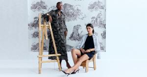 wo models posing in a studio with a leopard print backdrop, one standing beside an easel in a long patterned dress, and the other seated in a black dress with a light jacket.