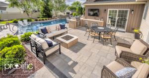 Backyard outdoor living space with a swimming pool, stone patio, modern outdoor kitchen with grill and TV, dining table with chairs, cushioned seating around a fire pit, and lush landscaping