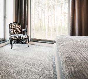 Hardwood Galleria Design Center is expanding its home improvement offerings with premium luxury carpet solutions for local properties Chair on carpet next to a bed.