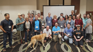 Group photo of CHM family members posing together at a CRF regional meeting, smiling and standing in a conference or meeting space.
