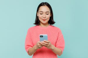 Asian American woman with short dark hair, on a turquoise background in a coral colored top. She is looked down at her smart phone.