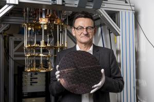 Diraq CEO and Founder Andrew Dzurak standing in front of cryogenic apparatus and holding a silicon wafer containing quantum computer chips