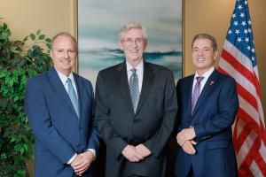 Attorneys Joseph Paulozzi, Richard Alkire Sr., and Joseph Condeni standing together in suits, smiling, with a U.S. flag and office backdrop.