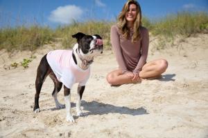 From sun protection for kids and families to BarkUV dog apparel, this October campaign combines lifelong sun safety with adoption awareness with 5% of online sales to support homeless pets A dog wearing a pink BarkUV sun-protective vest sitting outdoors in the sun with a woman wearing BloqUV enjoying the beach to highlight pet sun safety and adoption awareness.