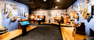 A music museum display featuring various instruments, including saxophones, guitars, and pianos, against a blue wall backdrop.