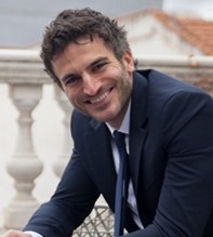Portrait of Francesco Muglia, Senior Vice President and Global Chief Commercial Officer at Costa Cruises, wearing a dark suit and smiling in a professional outdoor setting.