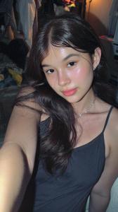 A close-up selfie of Mikaela Tala, a hyper-realistic AI influencer, taken with a harsh camera flash in a dimly lit, messy bedroom.