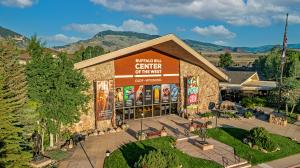 Photo of the facade of the Buffalo Bill Center of the West showing the entrance and names of the 5 museums and McCracken Research Library, as well as two large vertical banners