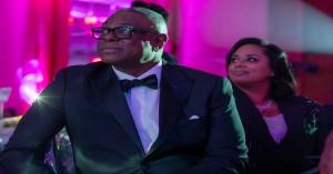 Dr. Wayne Purboo in a tuxedo and Dr. Nigela Purboo seated beside him at a gala with pink lighting.