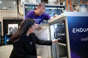 A scientist activates a diagnostic device inside of a hydrogen production facility, while another smiling scientist observes