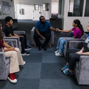 Teens are gathered around in comfy chairs for a group therapy session