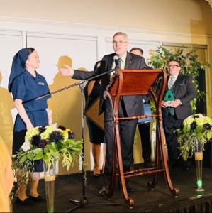 Maryvale President and CEO Steve Gunther speaking at the podium while introducing Sister Vika Meil, Daughter of Charity and board member, during the 2025 San Gabriel Valley Economic Partnership Emerald City-themed Awards Gala.
