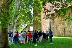Visitors attending a guided tour at Abbazia di Santa Giustina Villa Badia Sezzadio standing beneath large plane trees beside the historic brick façade in Sezzadio Piedmont Italy