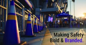 A row of purple and gold JBC traffic cones lines a sidewalk outside a modern event venue at sunset. Text reads Making Safety Bold & Branded. People and tents appear in the blurred background under warm lighting.