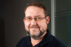 Author J. D. Edwards holding a copy of his book "The Scions of Faerie", with a backdrop of lush, mystical forest imagery.