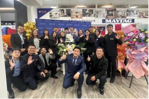 A group of Future Appliances employees and guests pose together indoors during the Grand Opening celebration, surrounded by flowers and decorations, smiling and giving thumbs-up gestures.