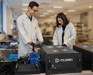 Two technicians in lab coats and PPE use an industrial device