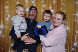 Two adults hold two young children in front of a gold starry backdrop; one child holds a tablet device, showing a welcoming, sensory-friendly family photo experience.
