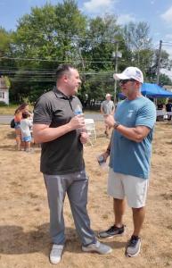 Dr. Andrew Van Scoyk stands on the left holding a water bottle while speaking with Dr. Kevin Greene, who is wearing a blue T-shirt and white cap. They are outdoors at an event with tents, chairs, and people in the background.