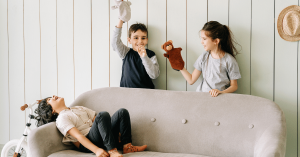Three children laughing and playing with hand puppets on a sofa inside a bright therapy room at Eastside Counseling Center, illustrating a warm and supportive environment for child and family counseling.