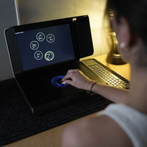 Woman completing a Cognivue cognitive test, turning the motorized dial as adaptive tasks for memory, focus, and reaction time display on the screen.