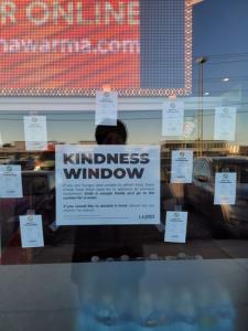Kindness Window covered with small kindness ticket cards around a central sign explaining how people in need can redeem a free meal and how others can donate.