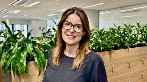 Daniella Muzitano, Executive Director of Titlespace, photographed in a modern office setting, wearing glasses and a black top, standing in front of indoor greenery.