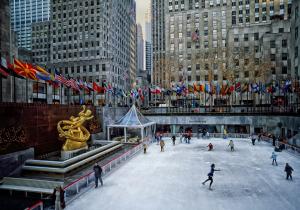 North Country Limousine Announces Seamless Holiday Transportation Solutions Connecting Suffolk County and NYC 7 Rockefeller Center ice skating rink in New York City with skaters, holiday lights, international flags, and the golden Prometheus statue.